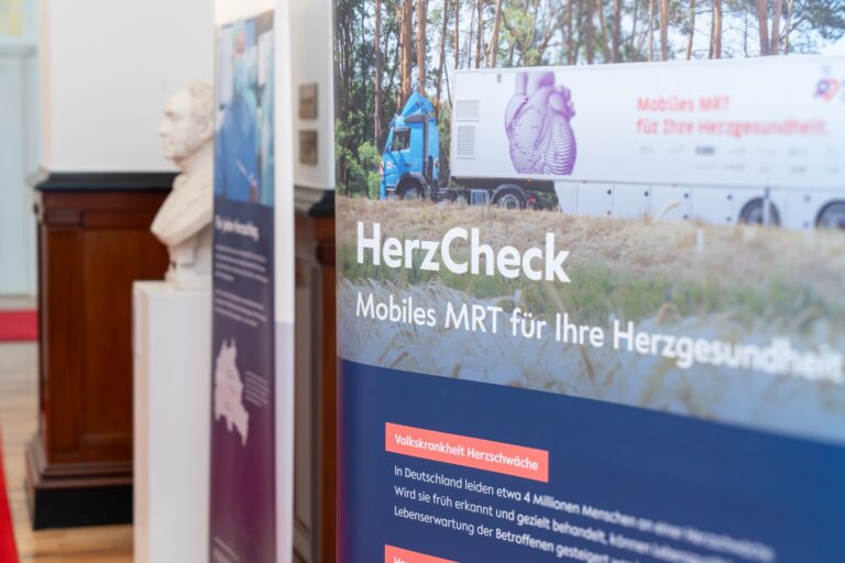 Werbeplakat für HerzCheck, ein mobiles MRT zur Herzgesundheit. Ein Truck mit großem Herzmotiv ist im Hintergrund abgebildet. Text informiert über Herzschwäche als Volkskrankheit in Deutschland und hebt die Bedeutung früher Erkennung hervor.